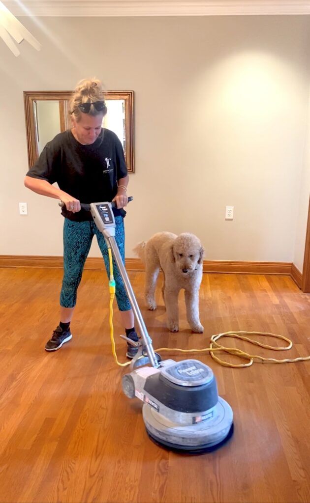 girl running a sanding machine over hardwood floor with dog looking on